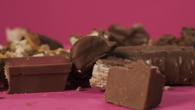 Mess with delicious and unhealthy chocolate bars smashed rotates on a pink background. Bitten sweets isolated. The unpacked bars are spinning. Nougat and caramel inside candy bar chocolate