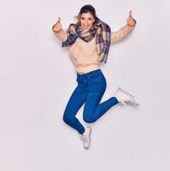 Young beautiful girl wearing winter clothes and scarf smiling happy. Jumping with smile on face...