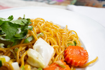 A closeup view of a plate of chow mein, in a restaurant or kitchen setting.