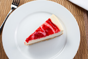 A top down view of a slice of strawberry swirl cheesecake on a plate, in a restaurant or kitchen setting.