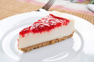 A view of slice of strawberry swirl cheesecake on a plate, in a restaurant or kitchen setting.