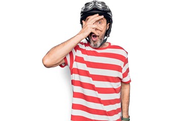 Middle age handsome motorcyclist man wearing moto helmet over isolated white background peeking in shock covering face and eyes with hand, looking through fingers afraid