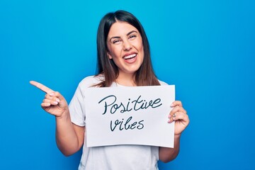 Young beautiful woman asking for optimist attitude holding paper with positive vibes message smiling happy pointing with hand and finger to the side