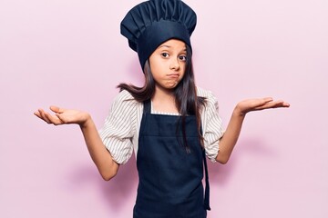 Beautiful child girl wearing cooker uniform clueless and confused with open arms, no idea and...
