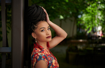 Stunning young biracial woman stands outside wearing standing at gate to small city park
