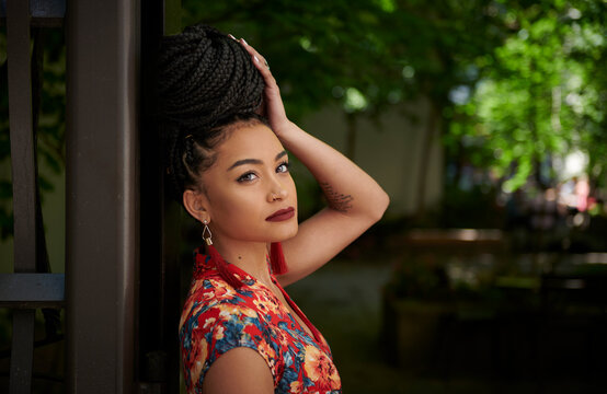 Stunning young biracial woman stands outside wearing standing at gate to small city park