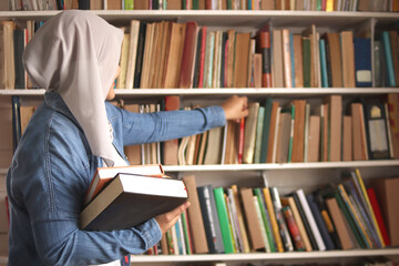 Asian muslim woman wearing hijab picking book in bookshelf, education concept, reading learning studying in library