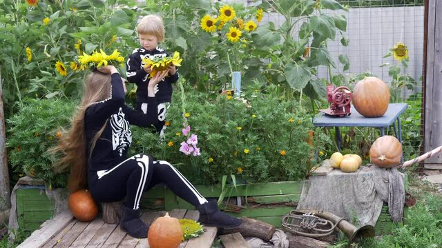 Happy blond boy plays with his sister against backdrop of flower garden with flowers decorated in form of boat. Brother and girls are dressed in carnival costumes of skeletons. Halloween eve. Close-up