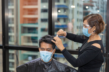 Young good looking male customer takes hair cut in a sky creeper business office while barber puts...