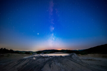 Milky way starry sky fading away into morning light with a muddy volcano in the foreground