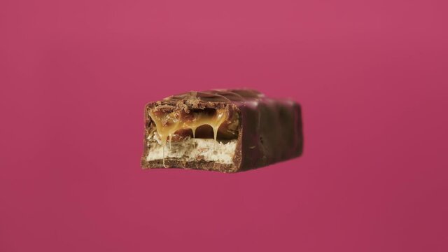 Bitten chocolate spin on isolate pink background. The unpacked bar is spinning. Nougat and caramel inside chocolate