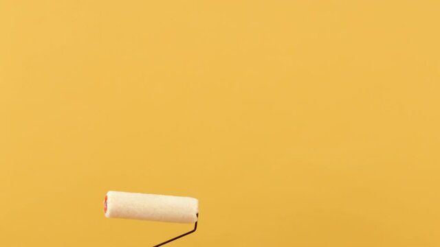 Woman hand holding paint roller moving up and down on empty space in yellow studio background