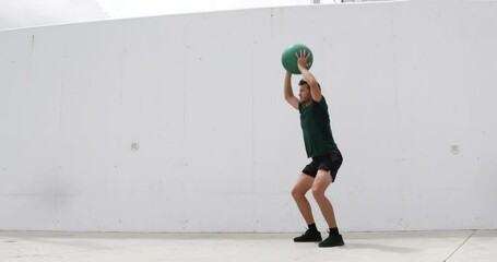 Squat with overhead medicine ball shoulder press. Weight exercises workout fitness man training legs and glutes with weighted medicine ball squats. Athlete working out at gym.