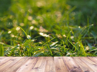 Wood table top over green grass field with sunlight in the morning for spring or summer background.