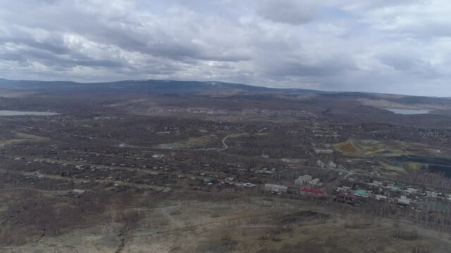 Panorama of Karabash city. Empty streets. Trees without leaves. Gloomy Ural mountains in the background. Chelyabinsk region, Russia. Aerial, spring, cloudy