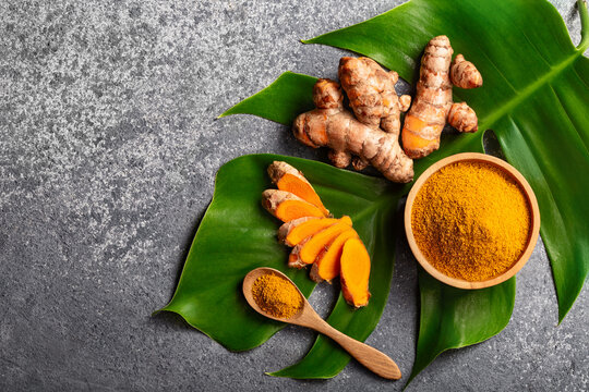 Turmeric powder and fresh turmeric root on grey concrete background with copyspace