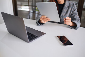 A businesswoman holding and using mobile  phone , tablet pc and laptop computer in office
