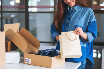 Closeup image of a woman opening and looking inside shopping bag with postal parcel box of clothing for delivery and online shopping concept