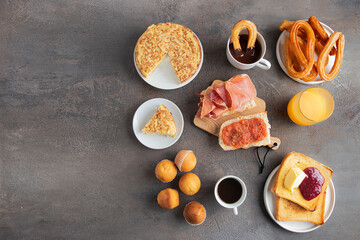 Different Spanish breakfast, tortilla, bruschetta with jamon (cured ham) and tomatoes, churros with chocolate,  Magdalena (Spanish cupcake) , frech toast with butter and jam ,coffee and juice.