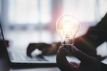 hand of a man with a light bulb and he is using a notebook computer. The idea of ​​inspiration...