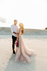 Fototapeta na wymiar Love Story of a beautiful couple in a pink wedding luxury dress with a bouquet in the Sahara desert, sand, dunes