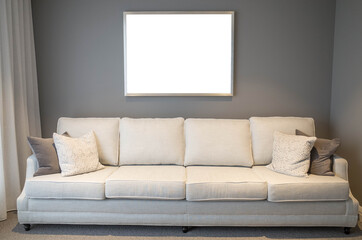 Blank white empty mock up template of a picture/art work with metal frame on living room/lounge wall with a neutral color sofa at front. Horizontal poster with copy space. Modern home/house interiors.