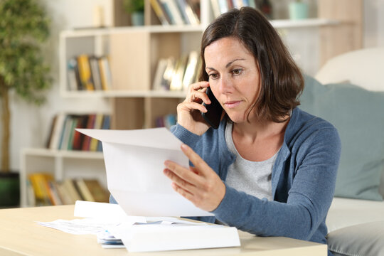 Serious adult woman checking letter calling on phone at home