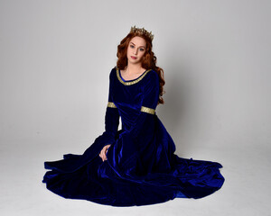 Full length portrait of  girl wearing long blue velvet gown with golden crown. sitting pose,...