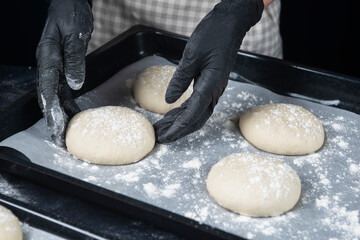 Woman in checkered apron and black gloves put a piece of yeast dough in baking tray. Process of making bakery. Adjarian Khachapuri Recipe – Georgian cheese bread.