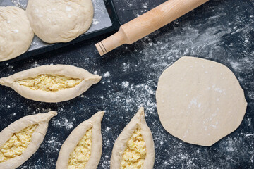 Rolled out piece of dough with a few ready raw khachapuri. Process of making bakery. Adjarian Khachapuri Recipe – Georgian cheese bread. Flat lay. Top view.