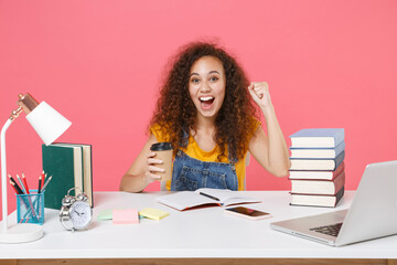 Excited african american girl employee in office isolated on pink background. Achievement business career. Education in school university college concept. Hold cup of coffee tea, doing winner gesture.