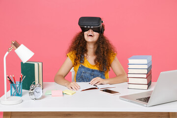 Cheerful african american student girl employee in office sit work at desk isolated on pink wall background. Business career. Education in school university college concept. Watching in pc headset