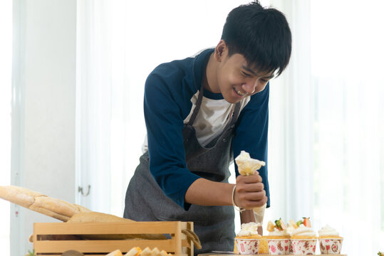 Asian teenager boy decorating cupcakes at home, lifestyle concept.