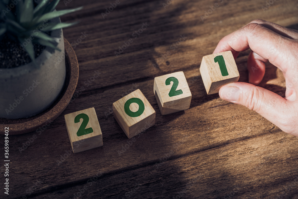 Aufkleber 2021 happy new year with hand pick up wood block on wood table with sunlight from window.hope for new year concept