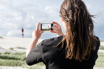 Reisende Frau, fotografiert Foto von einem Leuchtturm mit smartphone am Strand auf der Insel Amrum