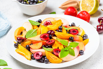 Fruit salad with berries in white plate, white background. Healthy vegan food concept.