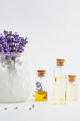 Lavender essential oil in small glass bottles and lavender flowers in mortar, white background.