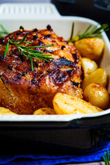 Baked pork loin with potatoes in an oven dish, black background.