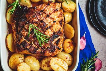 Baked pork loin with potatoes in oven dish, black background, top view.