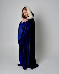 Full length portrait of  girl wearing long blue velvet gown with golden crown. sitting pose, isolated against a studio background.