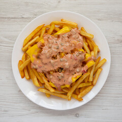 Homemade Animal Style French Fries on a white plate on a white wooden surface, top view. Flat lay, overhead, from above.