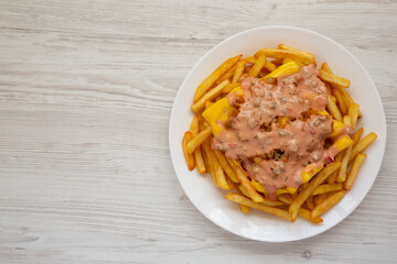 Homemade Animal Style French Fries on a white plate on a white wooden table, top view. Flat lay, overhead, from above. Copy space.