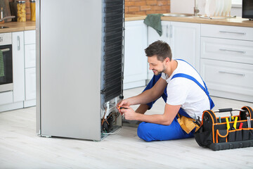Worker repairing refrigerator in kitchen