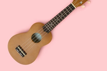 Flat lay of ukulele on a pastel pink background with place for text. Musical equipment.
