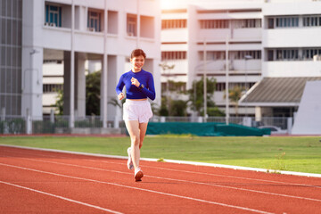 Fototapeta premium Young fitness woman runner jogging excercise in the morning on city stadium track in the city. Female athlete excercise in the city stadium to keep body fitness. Health and recreation stock photo.