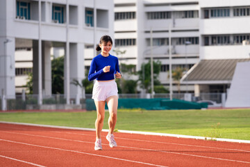 Fototapeta premium Young fitness woman runner jogging excercise in the morning on stadium track in the city. Female athlete excercise in the city stadium to keep body fitness during COVID-19 pandemic. Stock photo.