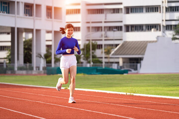 Young fitness woman runner jogging excercise in the morning on stadium track in the city. Female athlete excercise in the city stadium to keep body fitness during COVID-19 pandemic. Stock photo.