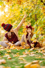 girls in the hat sit in autumn Park with maple leaf  and play, have fun.