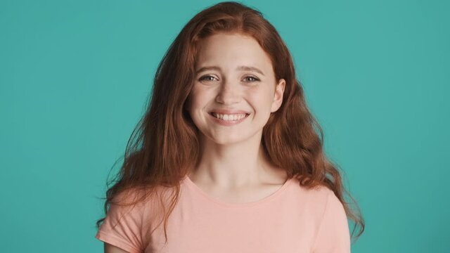 Attractive cheerful redhead girl surprisingly looking in camera and smiling over blue background. Happy expression