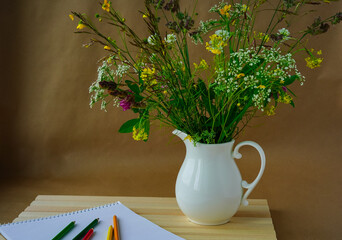 Bouquet of wildflowers in a beautiful jug, an album and pencils